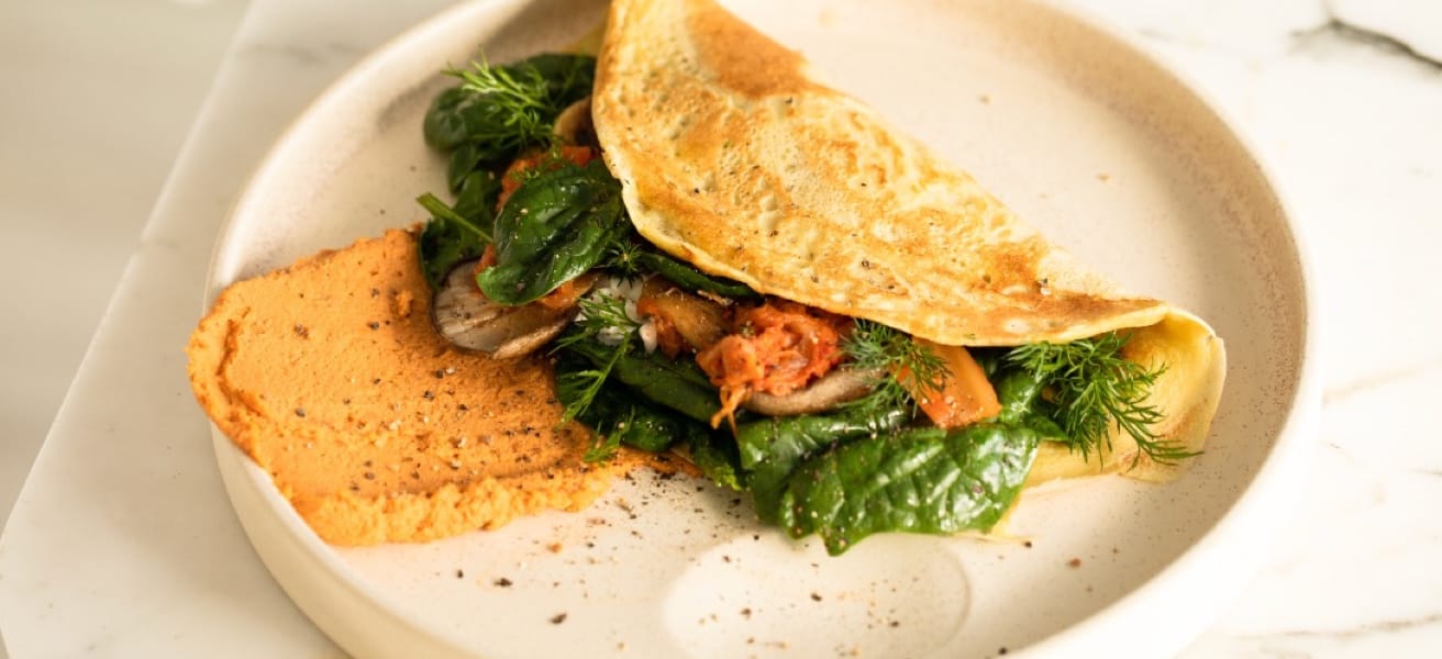 Cooked omelette filled with mushrooms, tomatoes, and green leaves with hummus next to it